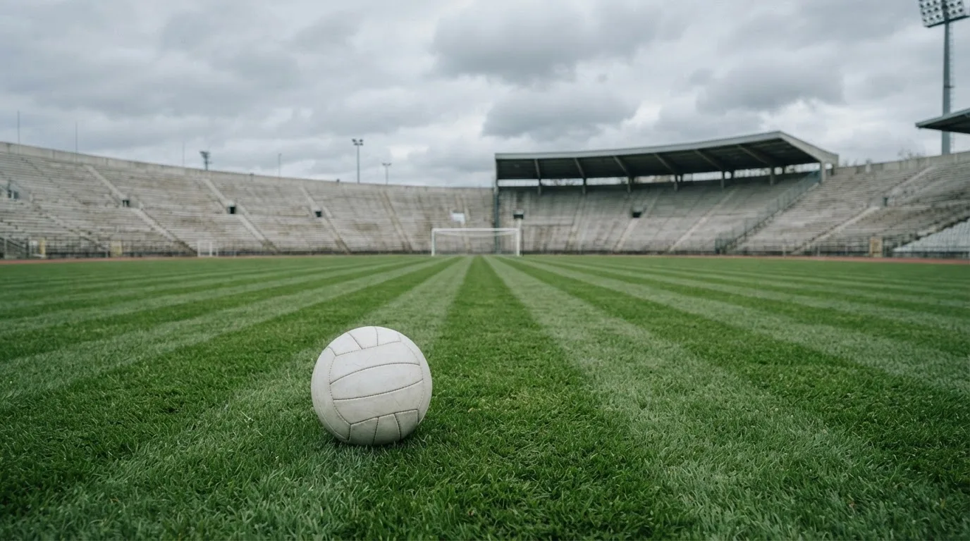 Ein Fußball auf einem Rasen, im Hintergrund ein leeres Stadion bei bewölktem Himmel.