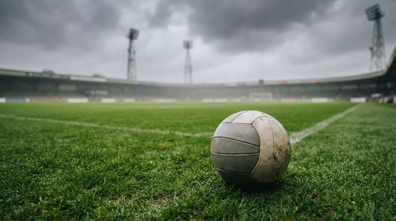 Ein Fußball auf einem Rasenplatz, im Hintergrund Flutlichtmasten und ein bewölkter Himmel.