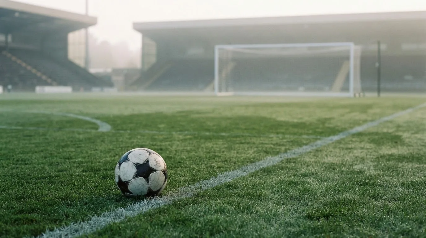 Ein Fußball auf dem Rasen vor einem leeren Tor im frühen Morgenlicht.