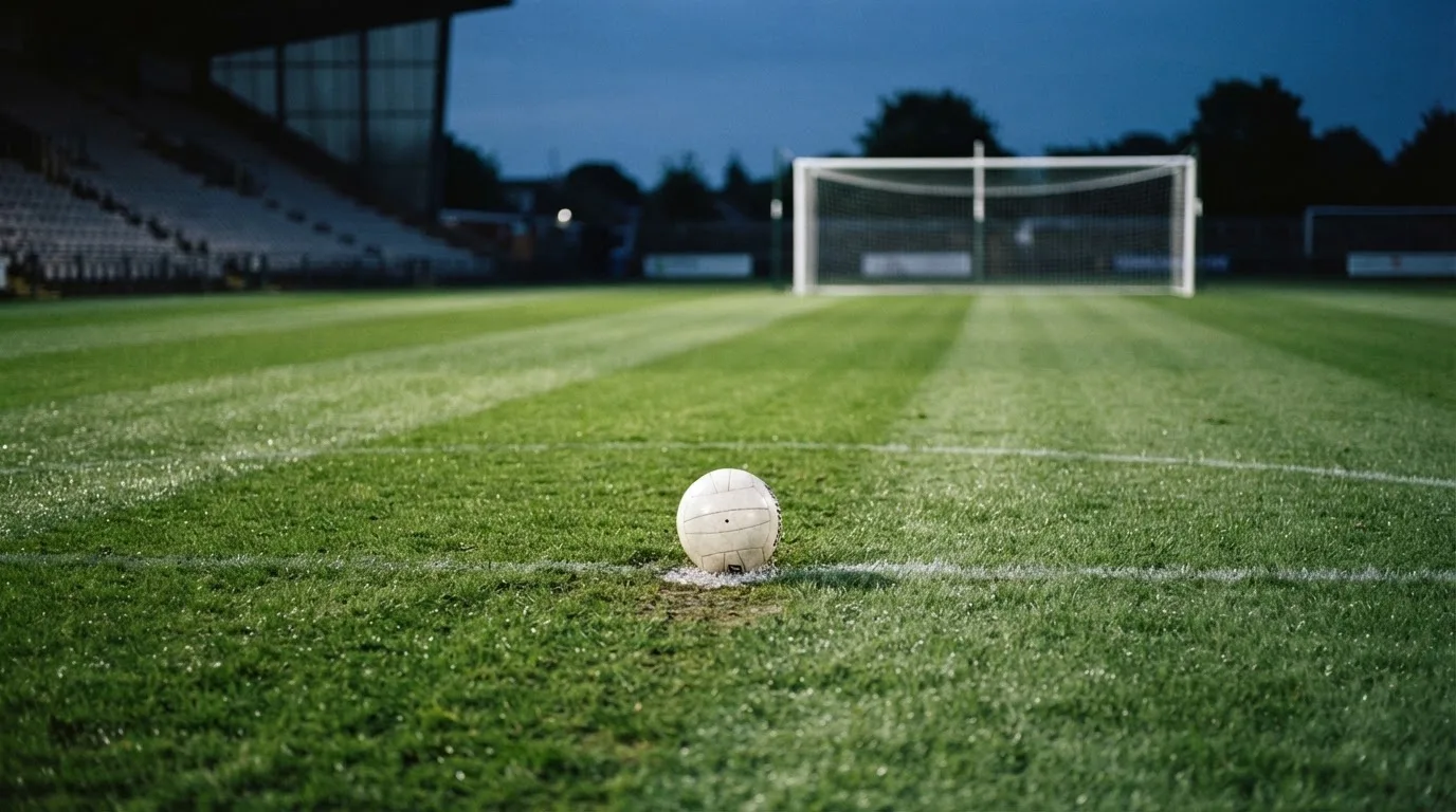 Ein Fußball liegt auf dem Elfmeterpunkt eines leeren Platzes im Abendlicht.