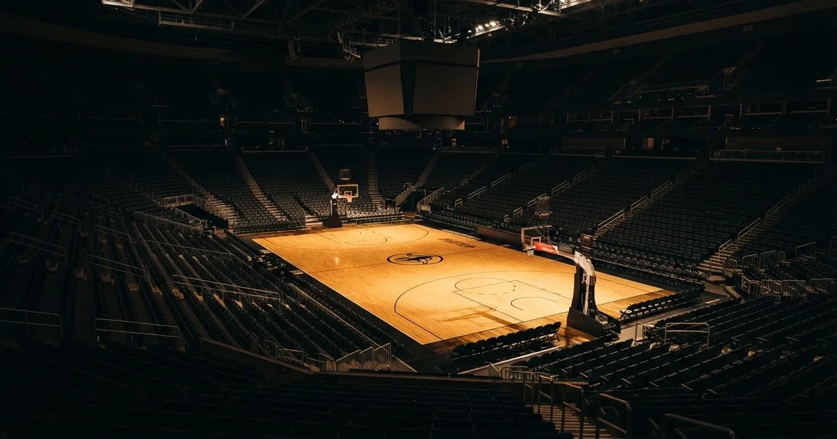 Eine leere Basketballhalle von einer oberen Tribünenreihe aus gesehen, Parkett und Körbe im Licht der Hallenstrahler.