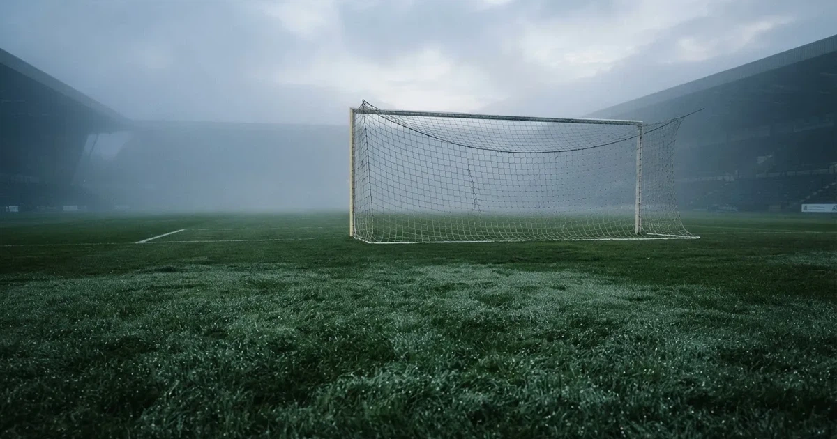 Ein Fußballtor mit Netz steht auf einem leeren Platz im Nebel der Morgendämmerung, der Rasen ist taufeucht.