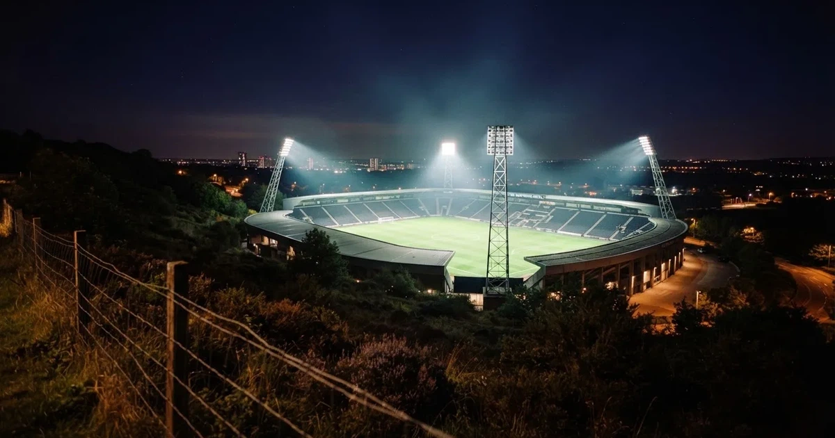 Ein Stadion bei Nacht unter Flutlicht aus der Ferne gesehen, der Rasen ist hell erleuchtet, keine erkennbaren Personen.