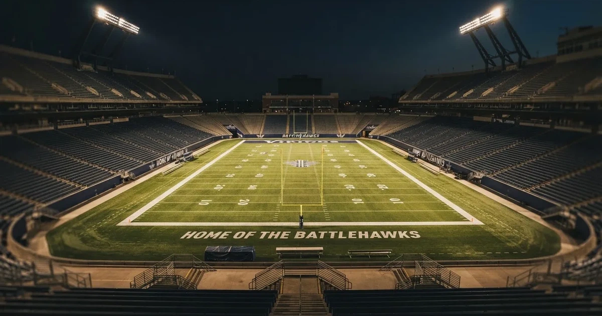 Ein American-Football-Feld mit weißen Yardlinien im Flutlicht, von einer hohen Tribüne aus gesehen, die Ränge leer, Zahlen nicht erkennbar.