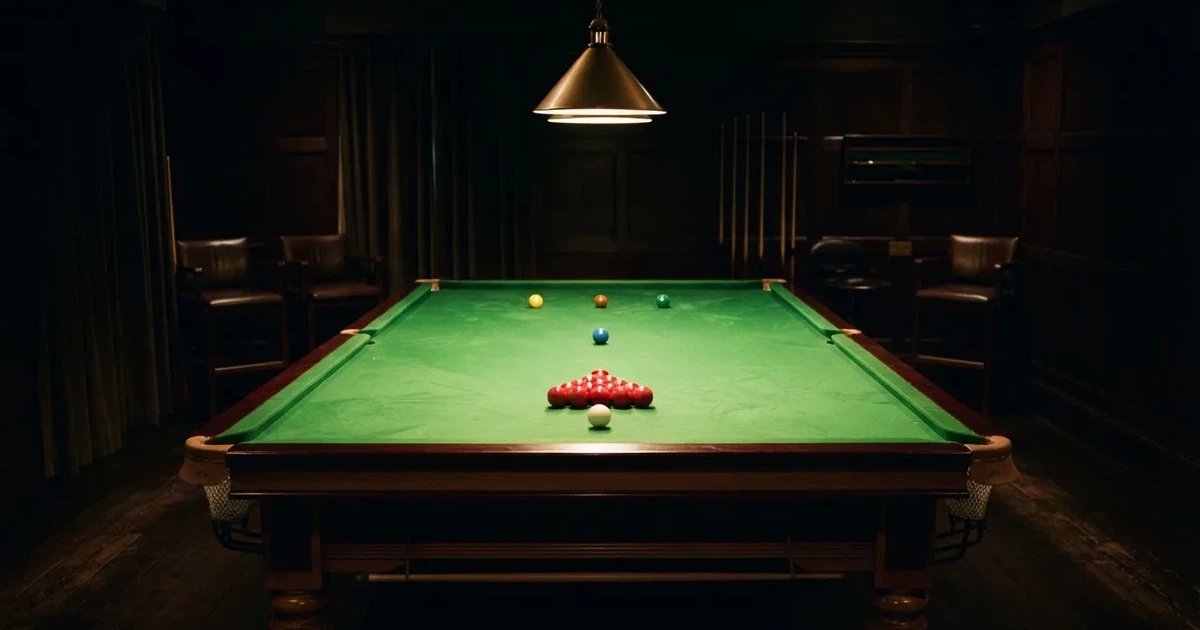 Ein Snookertisch mit grünem Tuch und aufgebauten roten Kugeln in einem abgedunkelten Raum unter einer hängenden Lampe.
