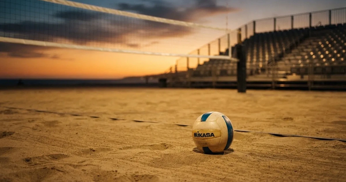 Ein Volleyball liegt auf dem Sand eines Beachvolleyball-Feldes neben dem gespannten Netz, im Hintergrund eine leere Tribüne bei Abendlicht.