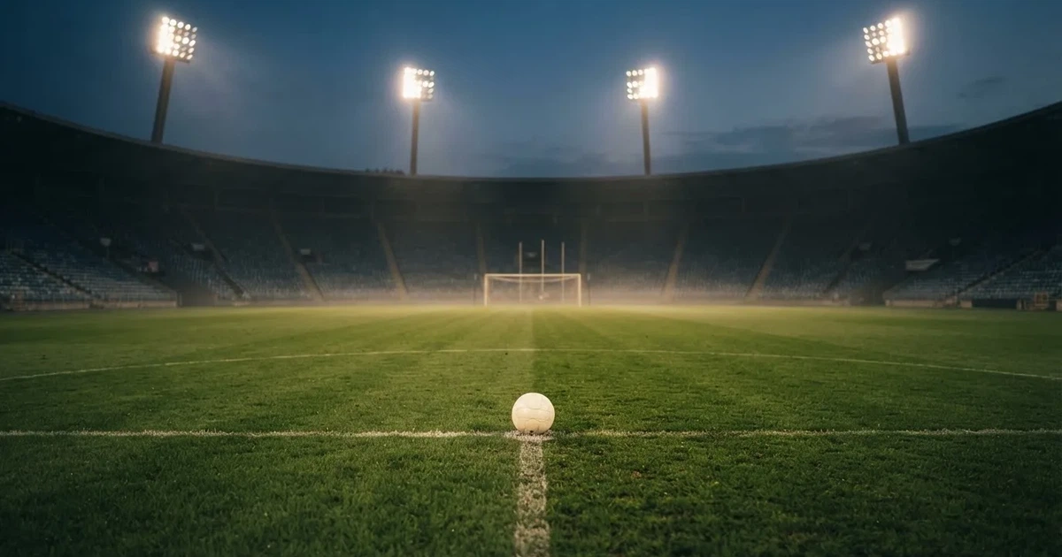 Ein Rasenplatz in der Dämmerung mit eingeschalteten Flutlichtmasten, ein Ball liegt am Anstoßpunkt, die Tribünen im Hintergrund sind unscharf.